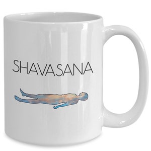 May include: White ceramic mug with the word "SHAVASANA" in black, above a watercolor illustration of a person in the corpse pose. The figure is in shades of blue, orange, and brown.