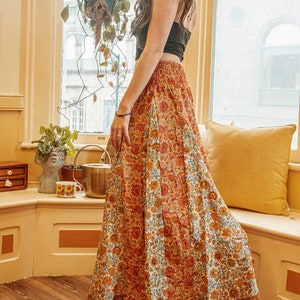 May include: A long, flowing skirt with a vibrant floral pattern in shades of orange, red, and blue. The skirt is paired with a black top. The skirt's design is reminiscent of bohemian or vintage styles.