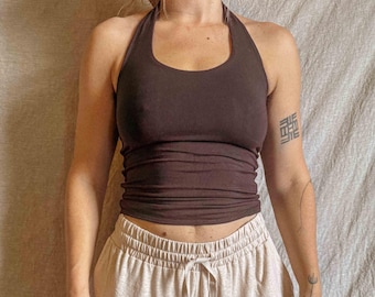May include: A dark brown halter top with a scoop neckline and a fitted silhouette paired with light beige wide-leg trousers featuring an elastic waistband and a matching drawstring cord with silver-toned metal aglets at the ends of the strings.