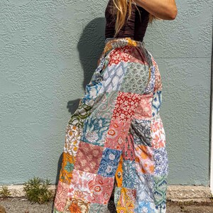 May include: Wide-leg trousers featuring a patchwork design composed of various floral and paisley patterns in shades of blue, red, orange, green, and white. The trousers have an elasticated waistband and a loose, flowing silhouette made of cotton fabric.