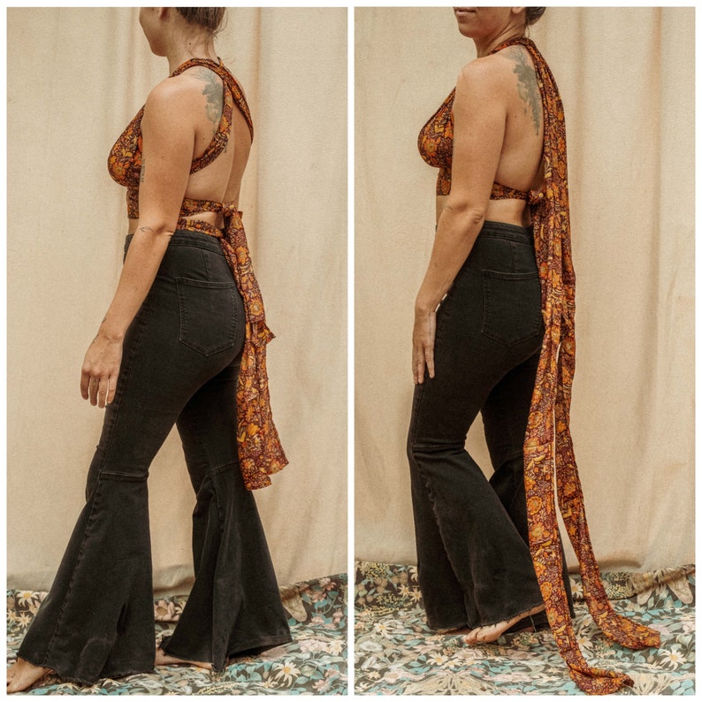 May include: A woman is wearing a black halter top with a colorful patterned fabric tied around her waist and a long scarf. She is also wearing black flared jeans.