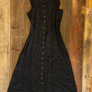 May include: A black sleeveless maxi dress with a button-up front and delicate embroidery. The dress has a flowy silhouette and a relaxed fit.
