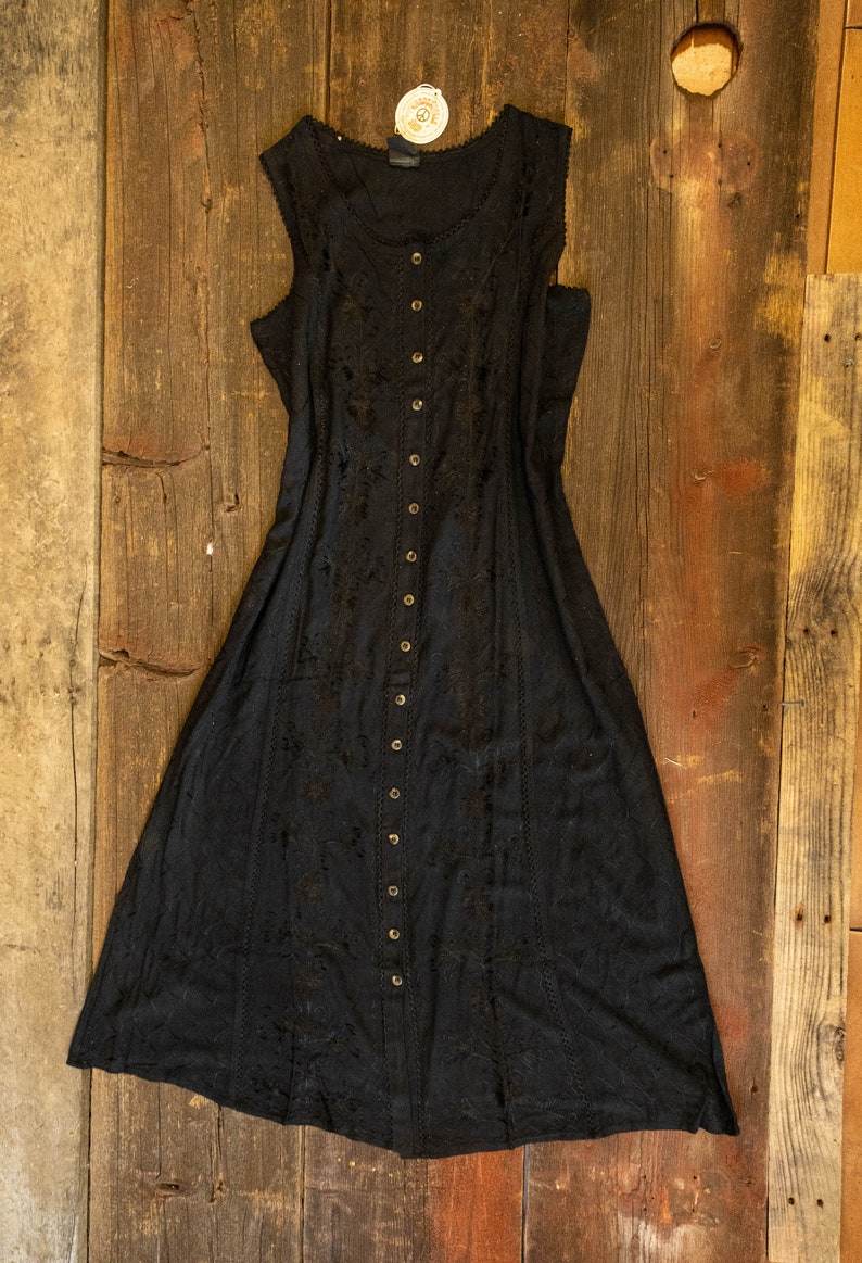 May include: A black sleeveless maxi dress with a button-up front and delicate embroidery. The dress has a flowy silhouette and a relaxed fit.