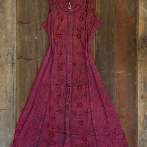May include: A long, sleeveless, burgundy dress with a button-up front and floral embroidery. The dress has a flowing, A-line silhouette.