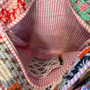 May include: A pink and white striped fabric bag with a patchwork design. The bag has a zipper closure and a small pocket inside. The bag is made of cotton and is perfect for carrying everyday essentials.
