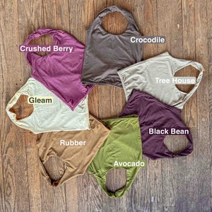 K&ouml;nnte beinhalten: Sieben &auml;rmellose Oberteile, die in einem Kreis angeordnet sind und jeweils mit einem Farbnamen beschriftet sind: Crushed Berry, Crocodile, Tree House, Black Bean, Avocado, Rubber und Gleam. Die Oberteile bestehen aus einfarbigem Stoff.