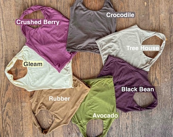 May include: Seven sleeveless tops arranged in a circle, each labeled with a color name: Crushed Berry, Crocodile, Tree House, Black Bean, Avocado, Rubber, and Gleam. The tops are made of a solid-colored fabric and feature a rounded neckline and armholes.