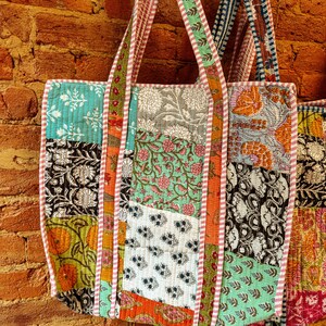 May include: A patchwork tote bag with a variety of colorful floral and geometric patterns. The bag has a long strap and is made of cotton fabric.
