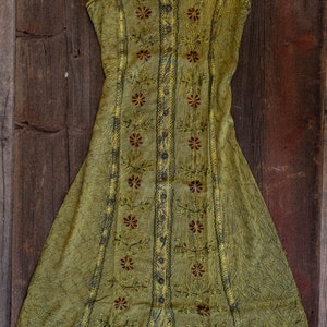 May include: A sleeveless, green, button-up dress with floral embroidery. The dress has a loose fit and a flowing skirt.