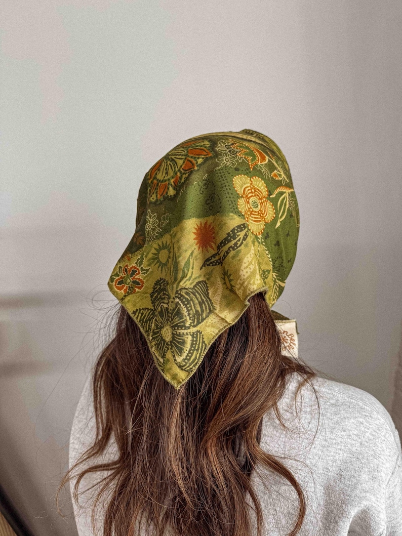 Puede incluir: Un pa&ntilde;uelo con estampado floral verde y amarillo. El cubrecabezas presenta una mezcla de dise&ntilde;os florales y geom&eacute;tricos en tonos verdes, amarillos y naranjas. El pa&ntilde;uelo est&aacute; atado en la parte posterior de la cabeza, con los extremos del pa&ntilde;uelo visibles.