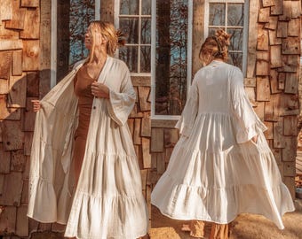 May include: A white, tiered, long-sleeved cotton robe with a button closure. The robe is flowy and has a relaxed fit.