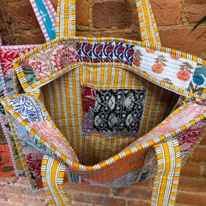 May include: A large, yellow and white striped tote bag made of patchwork fabric. The bag has a zipper closure and two long straps. The fabric is a mix of floral and geometric patterns in various colors.
