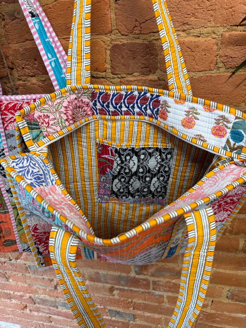 May include: A large, yellow and white striped tote bag made of patchwork fabric. The bag has a zipper closure and two long straps. The fabric is a mix of floral and geometric patterns in various colors.