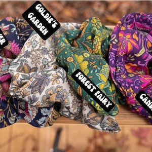 May include: Five colorful fabric scrunchies with floral patterns. The scrunchies are labeled "Wildflower", "Goldie's Garden", "Forest Fairy", "Candi Dreams", and "Zoey".
