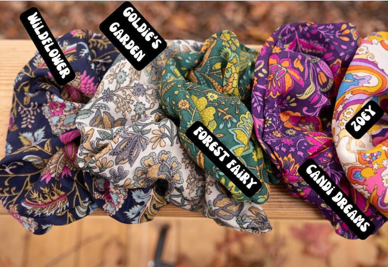 May include: Five colorful fabric scrunchies with floral patterns. The scrunchies are labeled "Wildflower", "Goldie's Garden", "Forest Fairy", "Candi Dreams", and "Zoey".