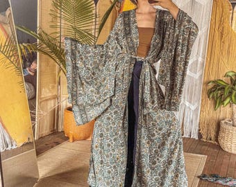 May include: A long, open-front kimono robe with a floral pattern in shades of green, brown, and cream. The robe is tied at the waist and worn over a brown top and dark pants. The sleeves are wide and flowing.