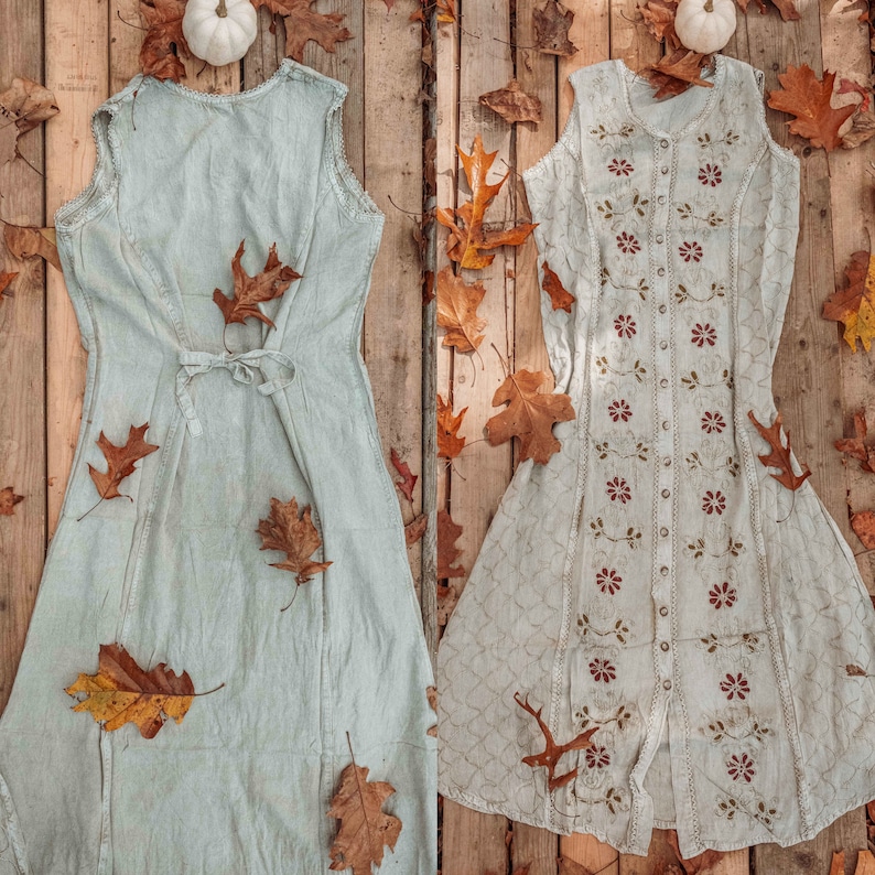 May include: Two white sleeveless dresses with different patterns and textures. The dress on the left is a simple, light blue dress with a tie at the waist. The dress on the right has a more intricate design with floral patterns and buttons down the front.