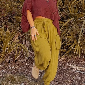 May include: A woman wearing a maroon, short-sleeved, loose-fitting top with a drawstring waist and olive green, loose-fitting trousers with a drawstring waist and pockets. She is wearing a silver peace sign necklace and a beaded necklace.