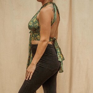 May include: A green and yellow floral print halter top with a tie back. The top is worn with black jeans.