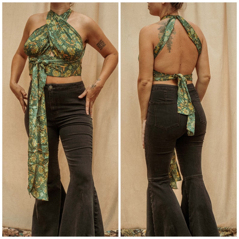 May include: A green and brown floral print halter top with a wrap style design. The top is tied at the back and the front. The model is wearing black flared pants.
