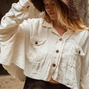 May include: A woman wearing a white, oversized button-down shirt with a brown woven sun hat. The shirt has two pockets and a frayed hem.