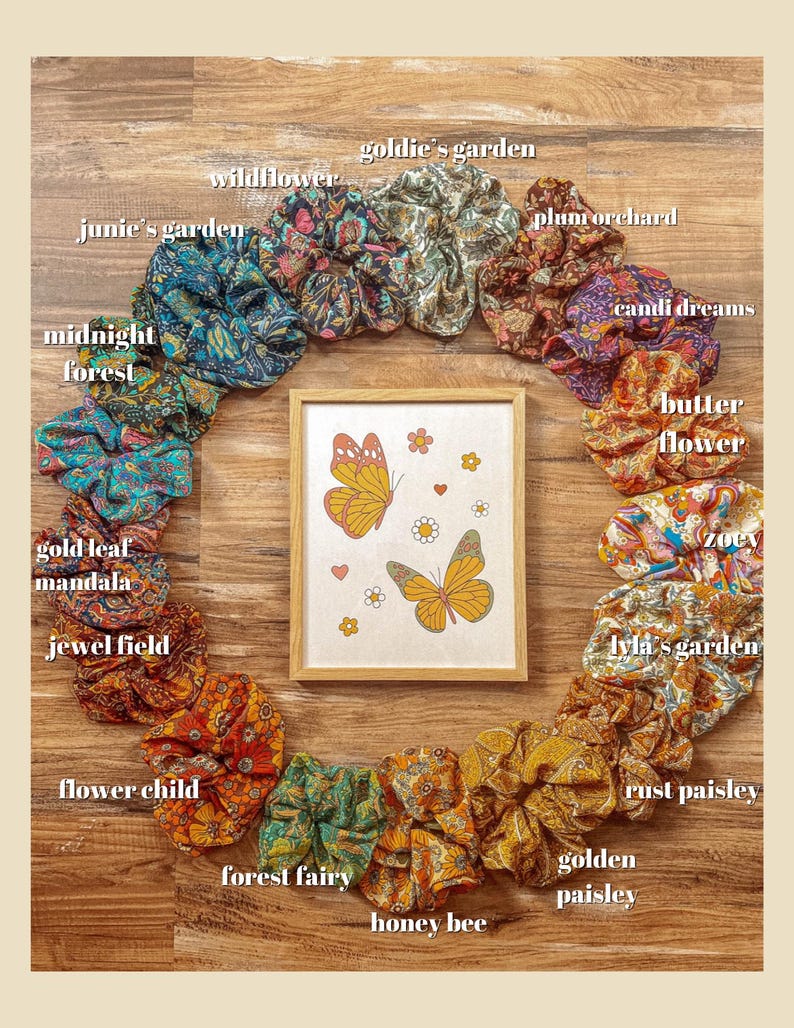 May include: A circle of colorful fabric scrunchies with floral patterns and names like "Goldie's Garden", "Wildflower", "Junie's Garden", "Midnight Forest", "Gold Leaf Mandala", "Jewel Field", "Flower Child", "Forest Fairy", "Honey Bee", "Golden Paisley", "Rust Paisley", "Lyla's Garden", "Zoev", "Butter Flower", "Candi Dreams", and "Plum Orchard". A framed picture of two butterflies with a floral background is in the center.