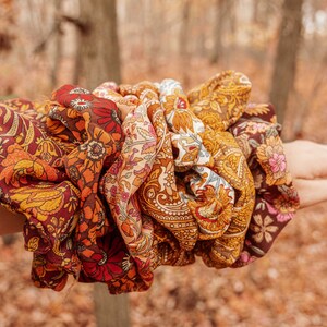 May include: A set of colorful patterned hair scrunchies in shades of brown, orange, yellow, and red. The scrunchies are made of fabric with a floral design.