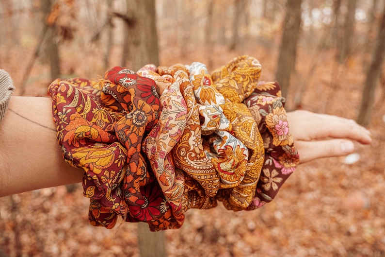 May include: A set of colorful patterned hair scrunchies in shades of brown, orange, yellow, and red. The scrunchies are made of fabric with a floral design.