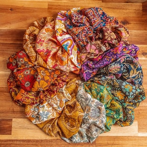 May include: A collection of colorful fabric scrunchies with floral patterns. The scrunchies are arranged in a circle on a wooden surface.