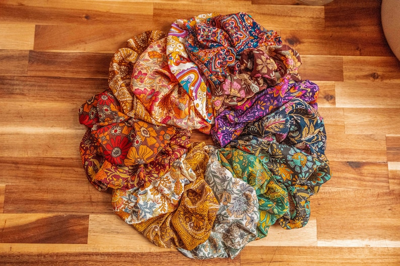 May include: A collection of colorful fabric scrunchies with floral patterns. The scrunchies are arranged in a circle on a wooden surface.