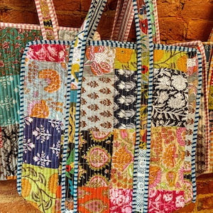 May include: Three colorful patchwork tote bags with blue and white striped straps. The bags are made of different fabrics with floral and geometric patterns.