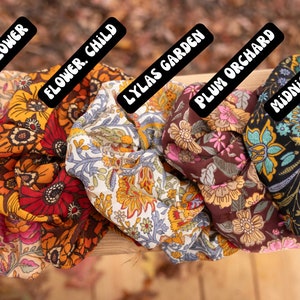 May include: Five colorful fabric scrunchies with floral patterns. The scrunchies are labeled "Butter Flower", "Flower Child", "Lylas Garden", "Plum Orchard", and "Midnight Forest".