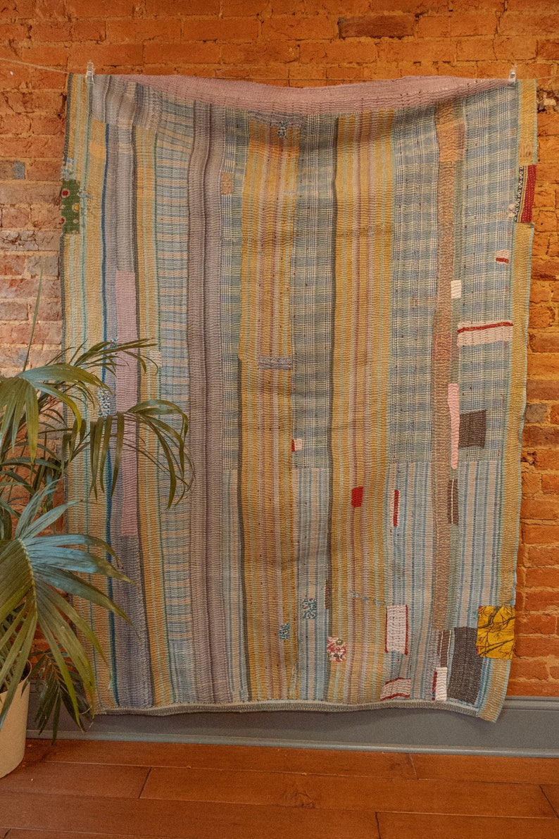K&ouml;nnte beinhalten: Ein Vintage-Kantha-Steppdecke mit Patchwork-Design mit blauen, gelben und rosa Streifen. Die Steppdecke ist aus recycelten Saris gefertigt und hat einen rustikalen, handgen&auml;hten Look.