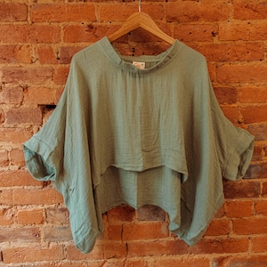 May include: A sage green, lightweight, loose-fitting, cropped top with a gathered neckline. The top has a relaxed, flowy silhouette and is made of a soft, breathable fabric.