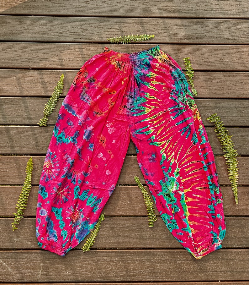 May include: Vibrant pink tie-dye trousers with a relaxed fit. The trousers display a colourful pattern of pink, blue, green, and yellow hues. The elasticated waistband and ankles provide a comfortable fit. Made from a lightweight fabric.