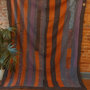 May include: A vintage quilt with a striped pattern in shades of orange, purple, and black. The quilt is made of different fabrics and has a rustic, handmade look.