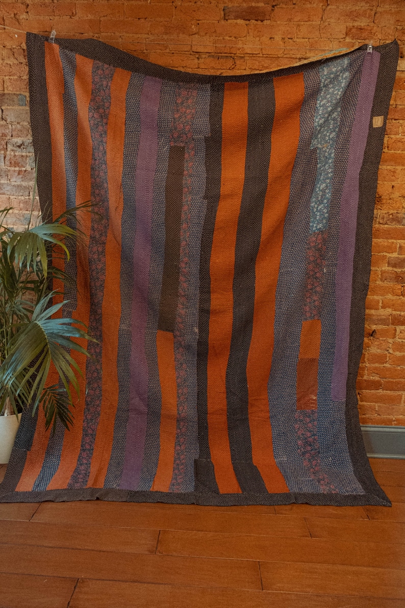 May include: A vintage quilt with a striped pattern in shades of orange, purple, and black. The quilt is made of different fabrics and has a rustic, handmade look.