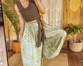 May include: A dark brown sleeveless wrap top with a side tie closure paired with loose-fitting, wide-leg pants featuring a light green and white tie-dye pattern with circular sunburst designs throughout the fabric.
