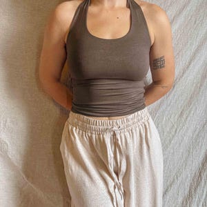 K&ouml;nnte beinhalten: Ein dunkelbraunes Neckholder-Top mit Rundhalsausschnitt und k&ouml;rpernaher Passform, kombiniert mit einer hellbeigen High-Waist-Freizeithose mit elastischem Bund und einem passenden Kordelzug in der vorderen Mitte des Kleidungsst&uuml;cks.