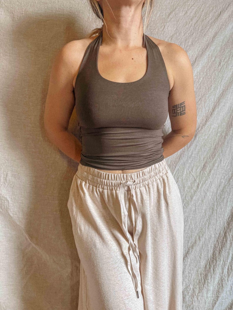 K&ouml;nnte beinhalten: Ein dunkelbraunes Neckholder-Top mit Rundhalsausschnitt und k&ouml;rpernaher Passform, kombiniert mit einer hellbeigen High-Waist-Freizeithose mit elastischem Bund und einem passenden Kordelzug in der vorderen Mitte des Kleidungsst&uuml;cks.