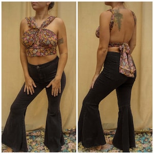 May include: A woman is wearing a black and white patterned halter top with a tie back. She is also wearing black flared pants.