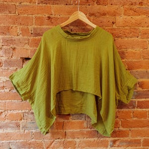 May include: A green, loose-fitting, short-sleeved top with a high, round neckline. The top is made of a soft, textured fabric and hangs loosely on a hanger.