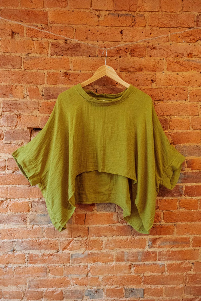 May include: A green, loose-fitting, short-sleeved top with a high, round neckline. The top is made of a soft, textured fabric and hangs loosely on a hanger.