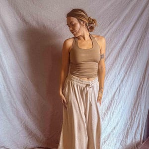 K&ouml;nnte beinhalten: Ein hellbraunes Neckholder-Top mit figurbetonter Passform kombiniert mit einer hellbeigen weiten Hose mit elastischem Bund und Kordelzug. Das Outfit besteht aus einem &auml;rmellosen Oberteil und einer weit geschnittenen Hose in neutralen Erdt&ouml;nen.