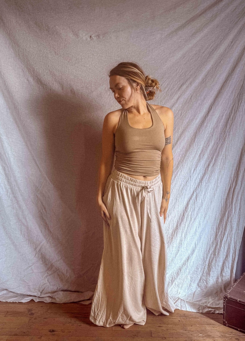 K&ouml;nnte beinhalten: Ein hellbraunes Neckholder-Top mit figurbetonter Passform kombiniert mit einer hellbeigen weiten Hose mit elastischem Bund und Kordelzug. Das Outfit besteht aus einem &auml;rmellosen Oberteil und einer weit geschnittenen Hose in neutralen Erdt&ouml;nen.