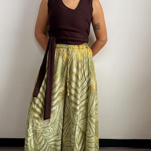Könnte beinhalten: Ein ärmelloses Wickeloberteil in Dunkelbraun, kombiniert mit einem langen, fließenden Rock. Der Rock hat ein grün-gelbes Batikmuster mit Blättern. Das Outfit ist lässig und bequem, geeignet für warmes Wetter.