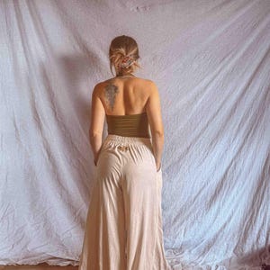 K&ouml;nnte beinhalten: Eine hoch taillierte Hose mit weitem Bein in hellem Beige, die ein kleines gesticktes Mottenmotiv am hinteren Bund aufweist. Die Hose hat eine lockere, flie&szlig;ende Silhouette mit Seitentaschen und einem elastischen Bund.