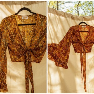 May include: Two long-sleeved tops with a tie front and bell sleeves. The top on the left is a yellow and brown floral print. The top on the right is a red and brown floral print.