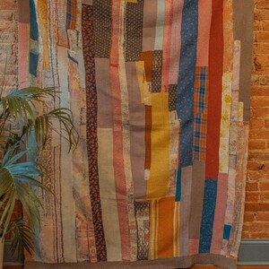 K&ouml;nnte beinhalten: Ein farbenfroher Patchwork-Deckenbezug mit vertikalen Streifen in Blaut&ouml;nen, Rot, Braun, Gelb und Rosa. Die Decke besteht aus verschiedenen Stoffen und Texturen, was ein einzigartiges und interessantes Design ergibt.