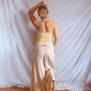 K&ouml;nnte beinhalten: Ein blassgelbes, tr&auml;gerloses Schlauchoberteil kombiniert mit einer locker sitzenden, cremefarbenen Hose mit weitem Bein. Die Hose verf&uuml;gt &uuml;ber einen elastischen Bund mit einem kleinen, gestickten Mottenmotiv mittig unter dem Bund.